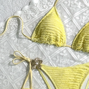 Detail of yellow pleated bikini with metal pearl flower accent on side tie