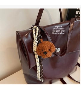 Detail of a brown teddy dog plush charm with tassel on a red leather handbag