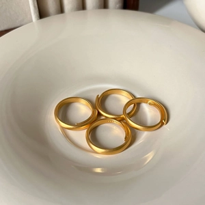 Set of four matte gold adjustable rings displayed in a white ceramic bowl