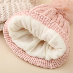 Pink cable-knit baby winter hat with plush fleece lining and fluffy pom-pom detail