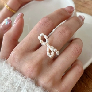 Close-up of baroque pearl bow ring worn by a model holding a white ceramic cup