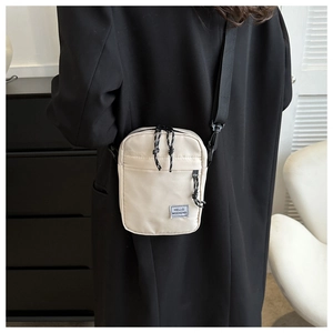 Détail d'un sac bandoulière en nylon beige avec étiquette HELLO WEEKEND porté par un mannequin