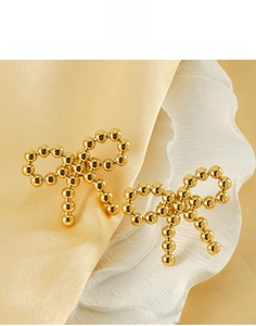 Detail of 18K gold bow knot earrings in titanium steel on a luxury ceramic display