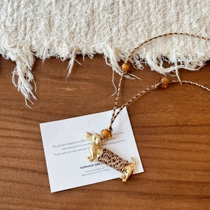 Détail du collier teckel tressé avec tête en métal doré et perles ambrées sur bois