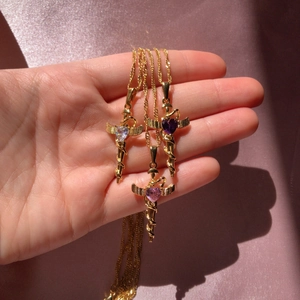 Detailed shot of gold winged heart necklaces with purple and pink gems on pink silk