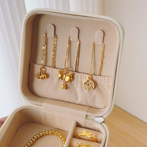 Portable beige jewelry organizer box displaying golden necklaces, bracelets and rings