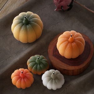 Five assorted pumpkin-shaped decorative candles in orange and white on a wooden base