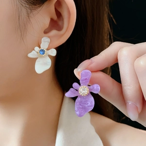 Gros plan de boucles d'oreilles fleurs en résine blanches et violettes avec détails zircon