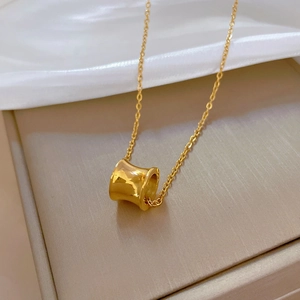 Macro detail of a polished gold cylinder pendant on a fine chain over white silk