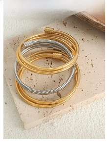 Detail view of gold and silver snake-bone coiled bracelets on a beige stone slab