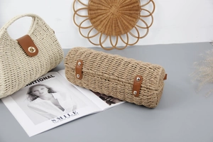 Detail of straw woven handbag featuring brown leather base straps and metal protective studs