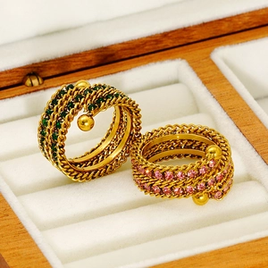 Detailed view of layered gold rings with green and purple gemstones in a wooden box