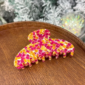 Close-up of a large mosaic hair claw clip in pink and yellow on a wooden tray