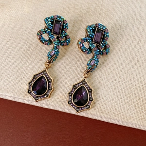 Détail de boucles d'oreilles vintage serpent dorées avec cristaux colorés et pendentifs