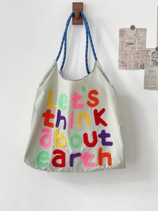 Detail of beige canvas tote with colorful towel embroidery text and blue woven straps