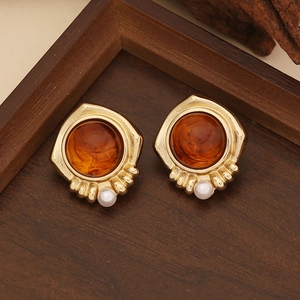 Vintage gold earrings with amber resin and white pearls on a dark wooden background