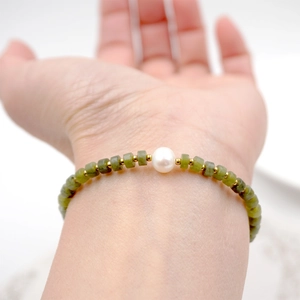 Bracelet en jaspe vert avec perle blanche centrale et entretoises dorées porté au poignet