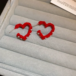 Vista macro di orecchini a cuore in floccato rosso con perle su vassoio in velluto grigio