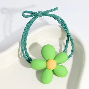 Close-up of a green flower hair tie with yellow stamen on a white heart-shaped plate