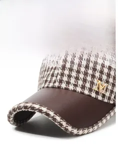 Detail of houndstooth baseball cap featuring brown leather brim and metal M logo buckle