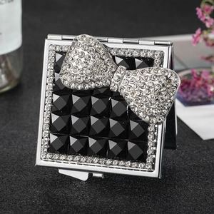 Square silver folding makeup mirror with luxury rhinestone bow on faceted black surface