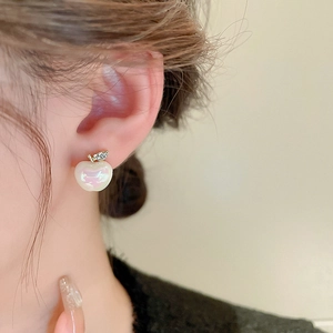 Close-up of pearlized apple stud earrings with gold leaf and sparkling rhinestone details