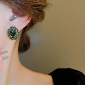 Macro detail of emerald green oval earrings with vintage gold settings and rhinestones