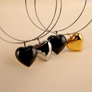 Minimalist heart pendant necklaces in black, silver and gold finishes on a beige background