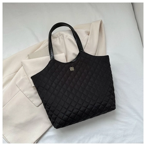 Détail du sac cabas matelassé noir avec logo trèfle doré sur un costume blanc