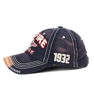 Détail des lettres FIRE brodées et de l'emblème d'aile sur la casquette en coton bleu