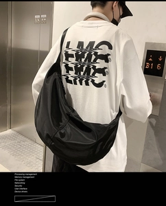 Street style view of the large black nylon crescent bag worn by a male model