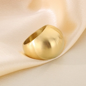 Close-up of a wide polished gold dome ring placed on elegant champagne silk fabric