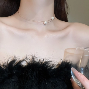 Close-up of a minimalist golden choker necklace with two pearls worn by a model