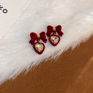 Macro di orecchini a fiocco in velluto rosso con ciondolo a cuore su morbido peluche