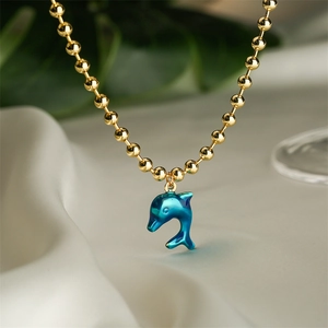 Detailed view of dolphin pendant necklace with gold beads on soft fabric background