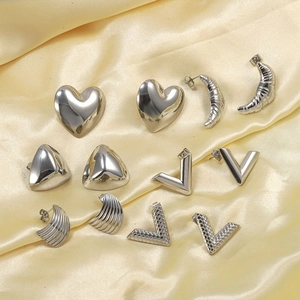 Close-up of six pairs of polished silver stainless steel earrings on yellow silk fabric
