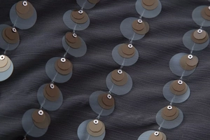 Close-up of layered brown sequins on dark gray mesh fabric with metallic ring accents