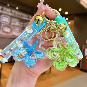 Detail of flower-shaped acrylic keychain with blue sand, starfish, and golden bell charm