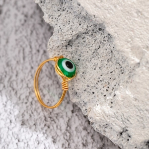 Macro detail of handmade gold wire-wrapped ring with a green evil eye bead on a stone