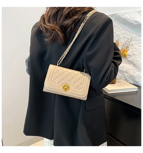 Detail of a beige quilted leather crossbody bag featuring a golden twist lock on a model