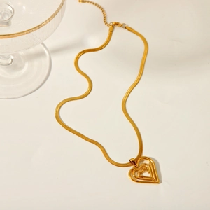 Collier chaîne serpent dorée avec pendentif triple cœur sur fond beige élégant