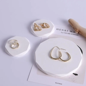 Minimalist geometric plaster jewelry stand with golden earrings and a bird-shaped ring