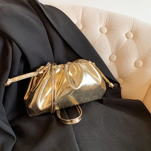 Metallic gold pleated cloud bag with slim shoulder strap on black suit and beige sofa background