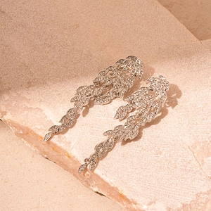 Close-up of silver leaf tassel earrings with sparkling rhinestones on stone background