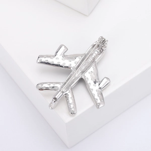 Detailed view of silver airplane brooch with snowflake pattern on white cube display