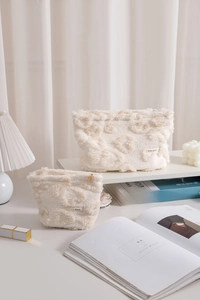 Set of two cream plush makeup bags with heart textures and H&R BAG labels on soft white background