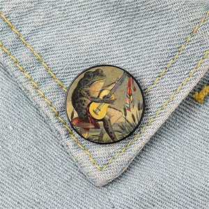 Close-up of a vintage frog playing guitar mushroom pin badge on light blue denim fabric