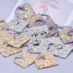 Macro shot of pentagon-shaped hammered metal earring charms in gold, silver, and rainbow