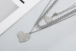 Detail of silver layered necklace featuring heart pendants and pearl cuban chain