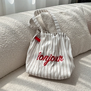 Close-up of striped canvas tote bag with red bonjour embroidery on a soft white sofa